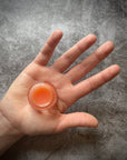An open glass pot of lip salve that is placed in the palm of a hand. 