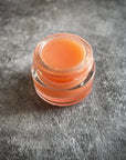 An open glass pot of pink lip gloss.