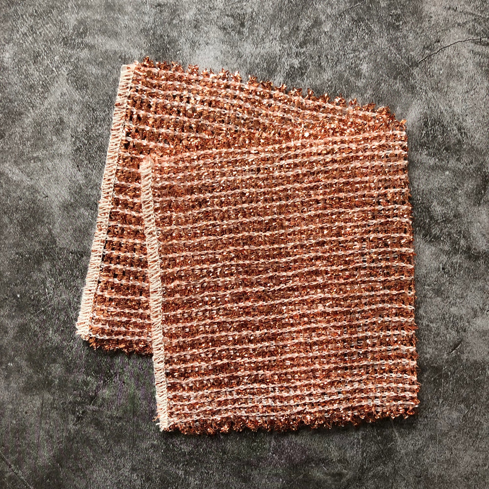 Two copper cleaning cloths on a gray surface