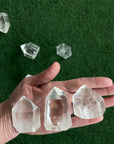 Three crystals are placed in the palm of a person's hand in front of a green surface. 