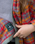 A close-up of a red plaid camp blanket that is wrapped around a persons shoulders. The Dig + Co. logo is displayed on the blanket. 