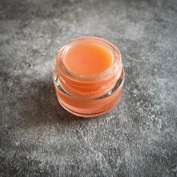 An open glass pot of pink lip gloss.