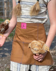 A person wears the canvas utility apron and holds two young chickens. 