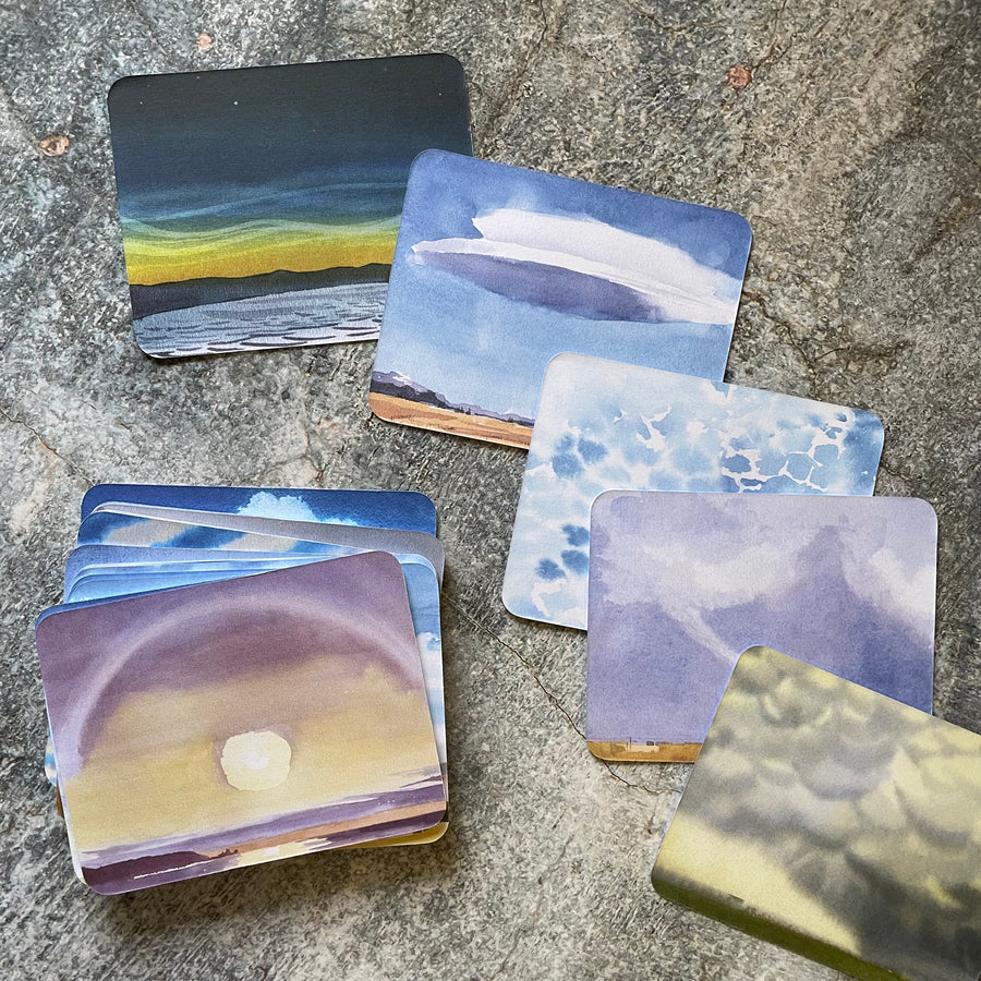 Watercolor illustrations on the back of the cards from the cloud spotter deck displayed on a gray surface. 