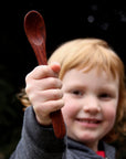 Redheaded toddler holding wooden spoon in front of face