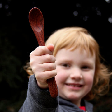Redheaded toddler holding wooden spoon in front of face