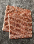 Two copper cleaning cloths on a gray surface 