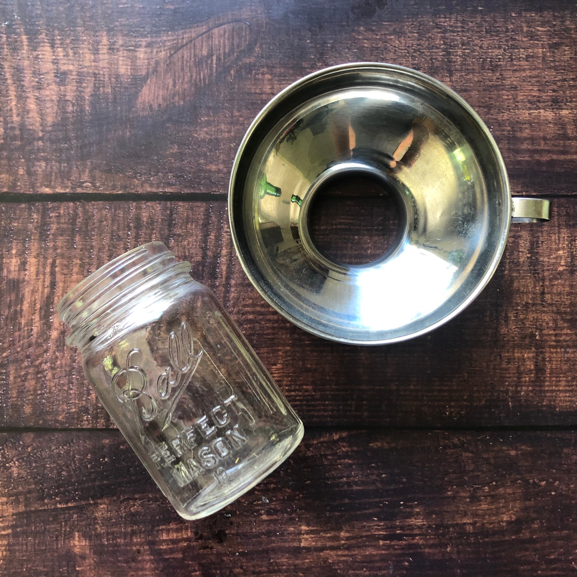 A stainless steel canning funnel and a glass jar are placed on a wooden surface. 