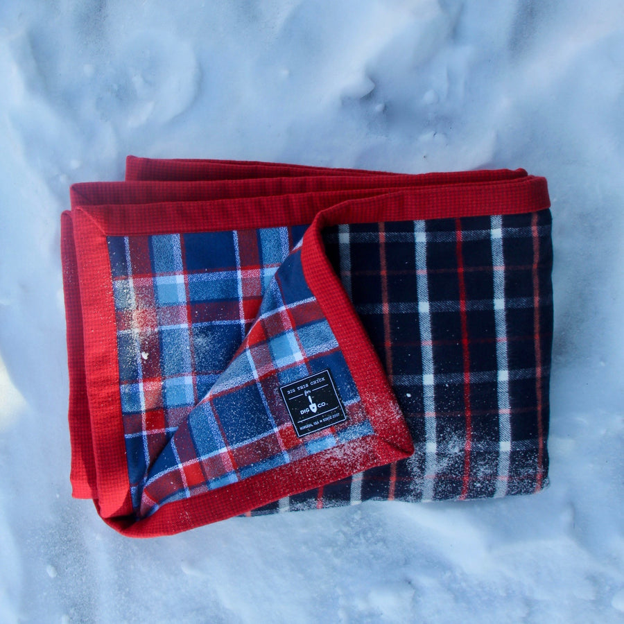 Folded blue and white flannel Camp Blanket folded and placed in the snow. 