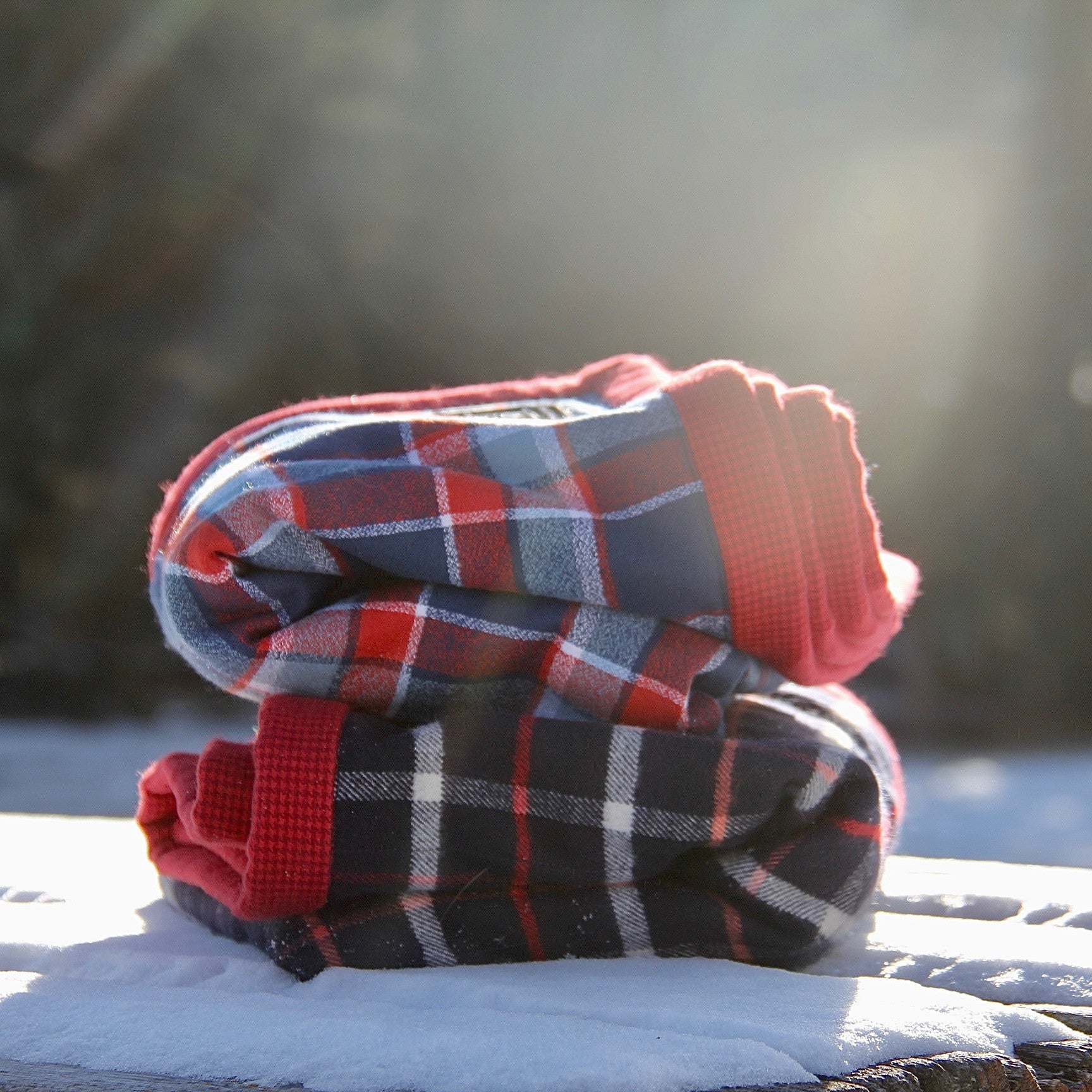 Folded handmade blue and red flannel camp blanket placed in the snow in the sunshine. 