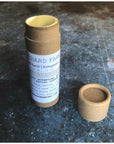 A brown tube of pearl luster brightening balm is standing upright and opened on a grey background. The cap lies to the side. 
