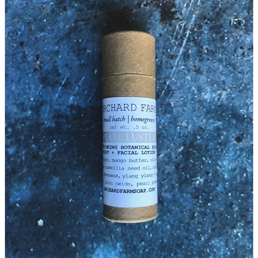 A brown tube of pearl luster brightening balm rests on a gray background. 