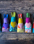 Six multicolored handmade fabric bunny rattles lie on a wooden surface. 