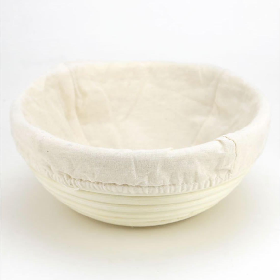 A bread proofing basket with a muslin liners sits with a white background.