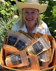 Terri Holt, standing in a garden,  looking up at the camera holding a basket of her handcrafted herb and spice blend.