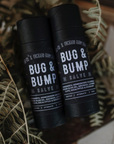 Two black tubes of Bug & Bump Salve are placed on small ferns. 