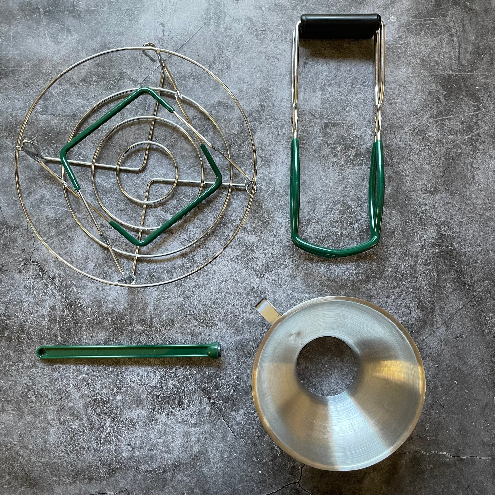 Contents of the Canning Gift Bundle displayed on a gray surface. Jar lifter, lid lifter, canning rack, and canning funnel. 