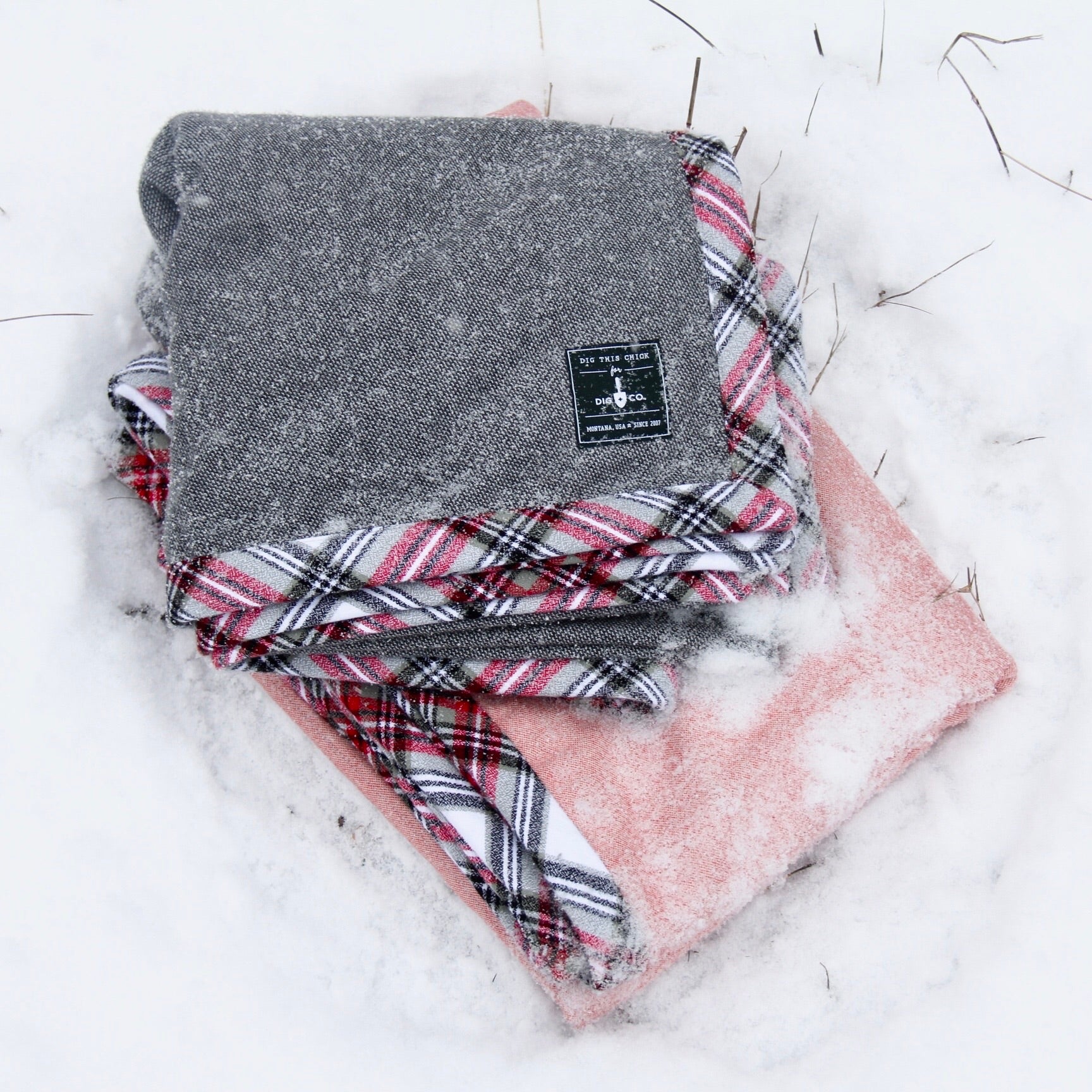 Two gray and pink handmade blankets with flannel trim are folded and lie in the snow. 