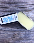 A tin of cuticle salve is opened and placed on a wooden surface 