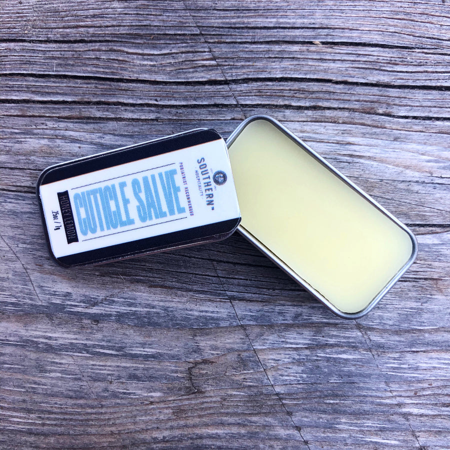A tin of cuticle salve is opened and placed on a wooden surface 