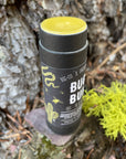 An open tube of bug and bump salve is placed on a rock outdoors next to a bright green piece of lichen. 