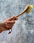 Hand holds up wooden dish brush in front of grey background