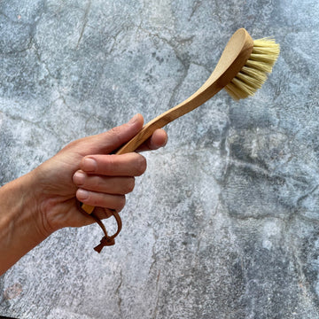 Hand holds up wooden dish brush in front of grey background