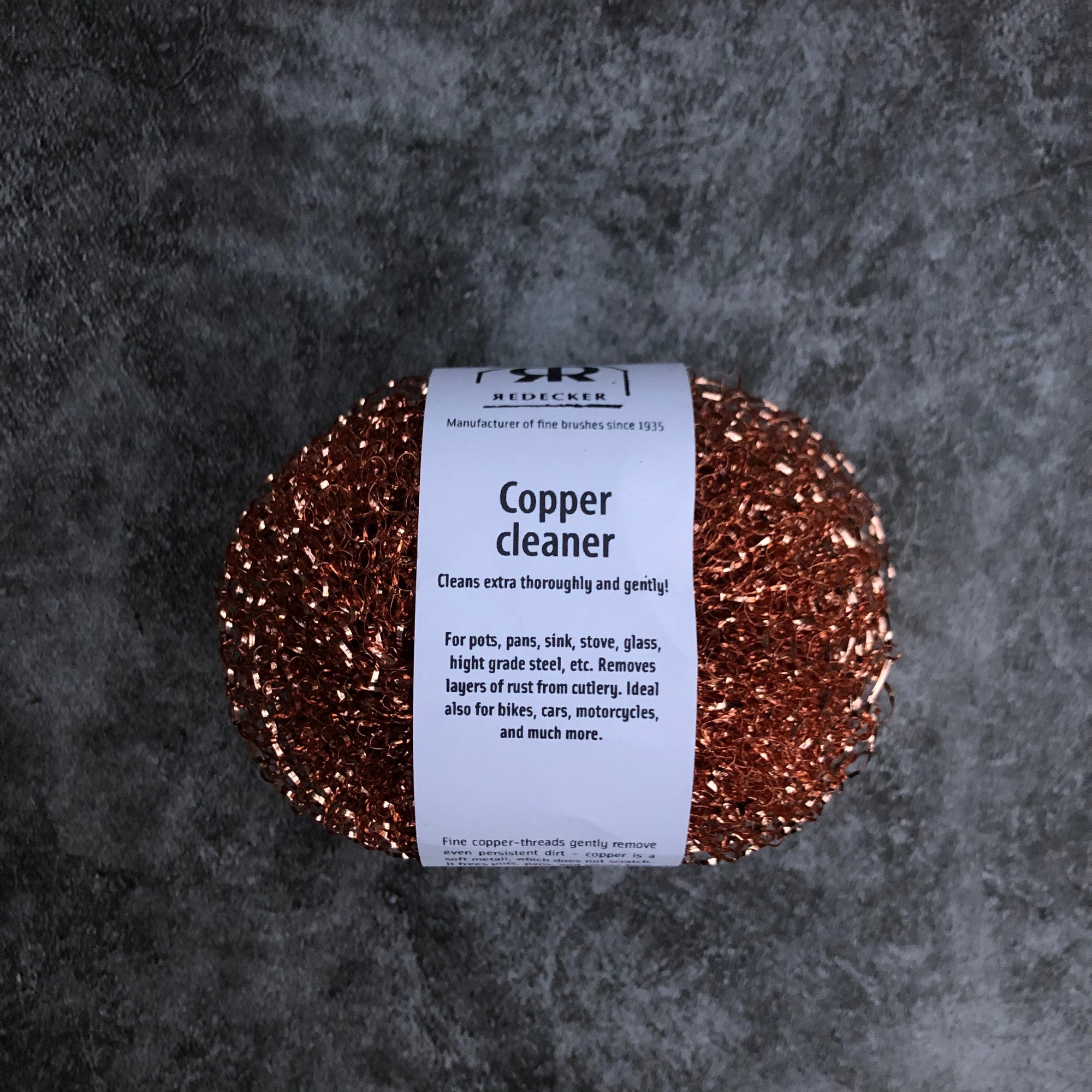 A pack of two copper pot scrubbers on a gray surface. 