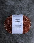 A pack of two copper pot scrubbers on a gray surface. 
