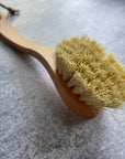 Close up of the bristles and handle of wooden dish brush in front of grey background