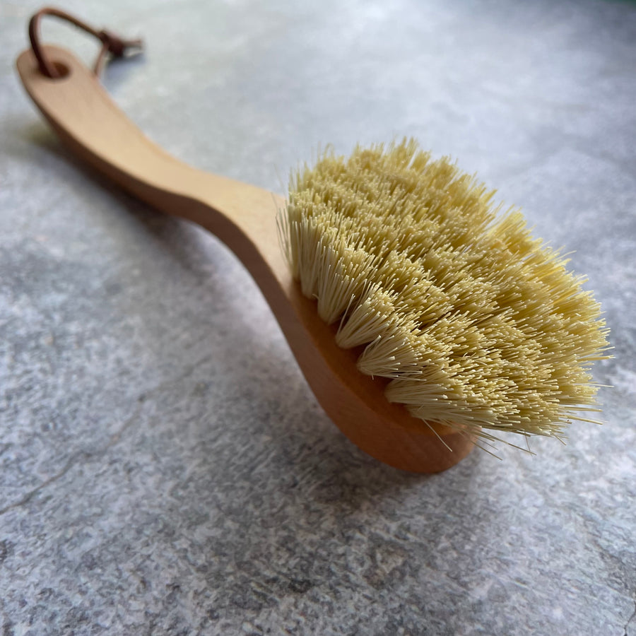 Close up of the bristles and handle of wooden dish brush in front of grey background