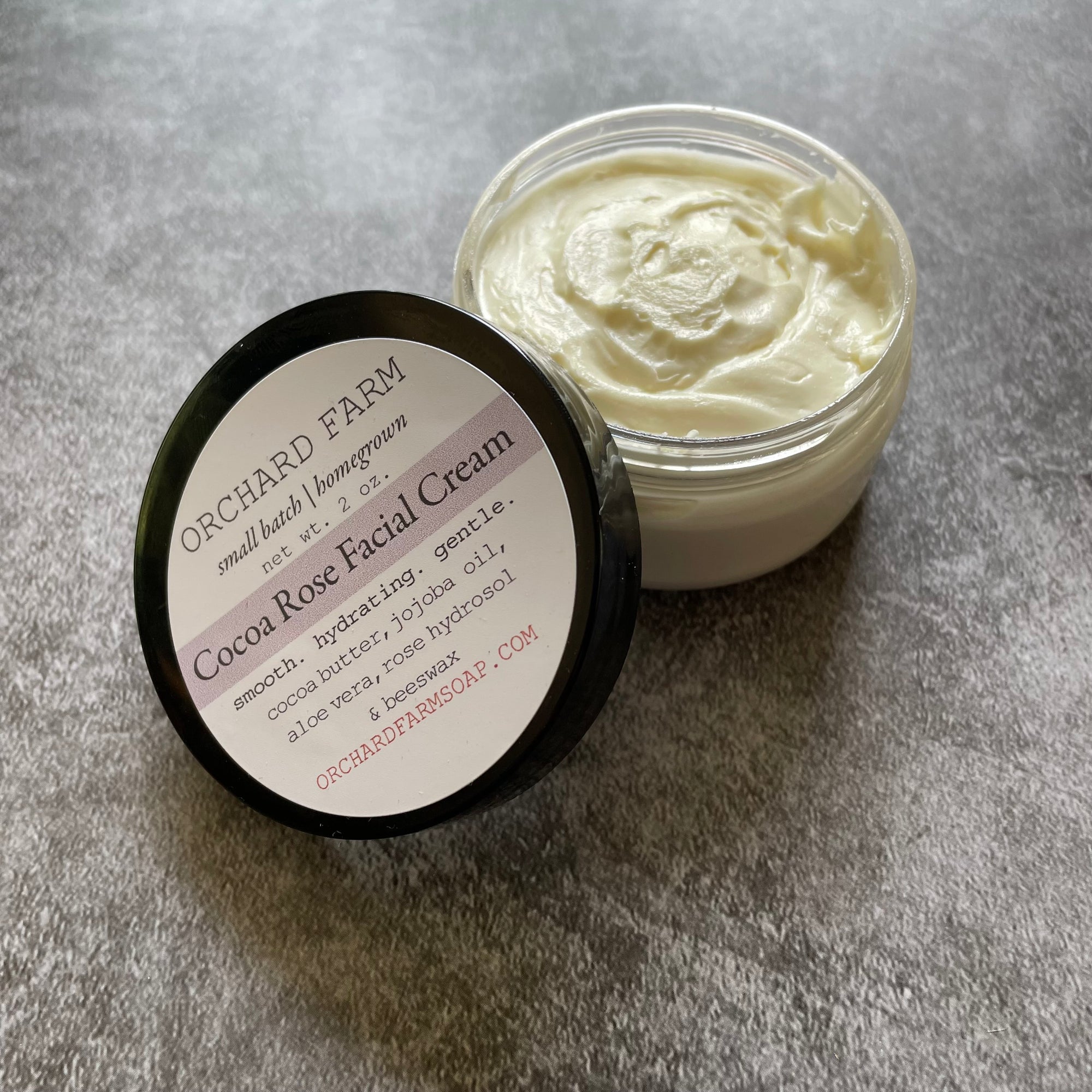 An open container of cocoa rose facial cream on a gray surface. 