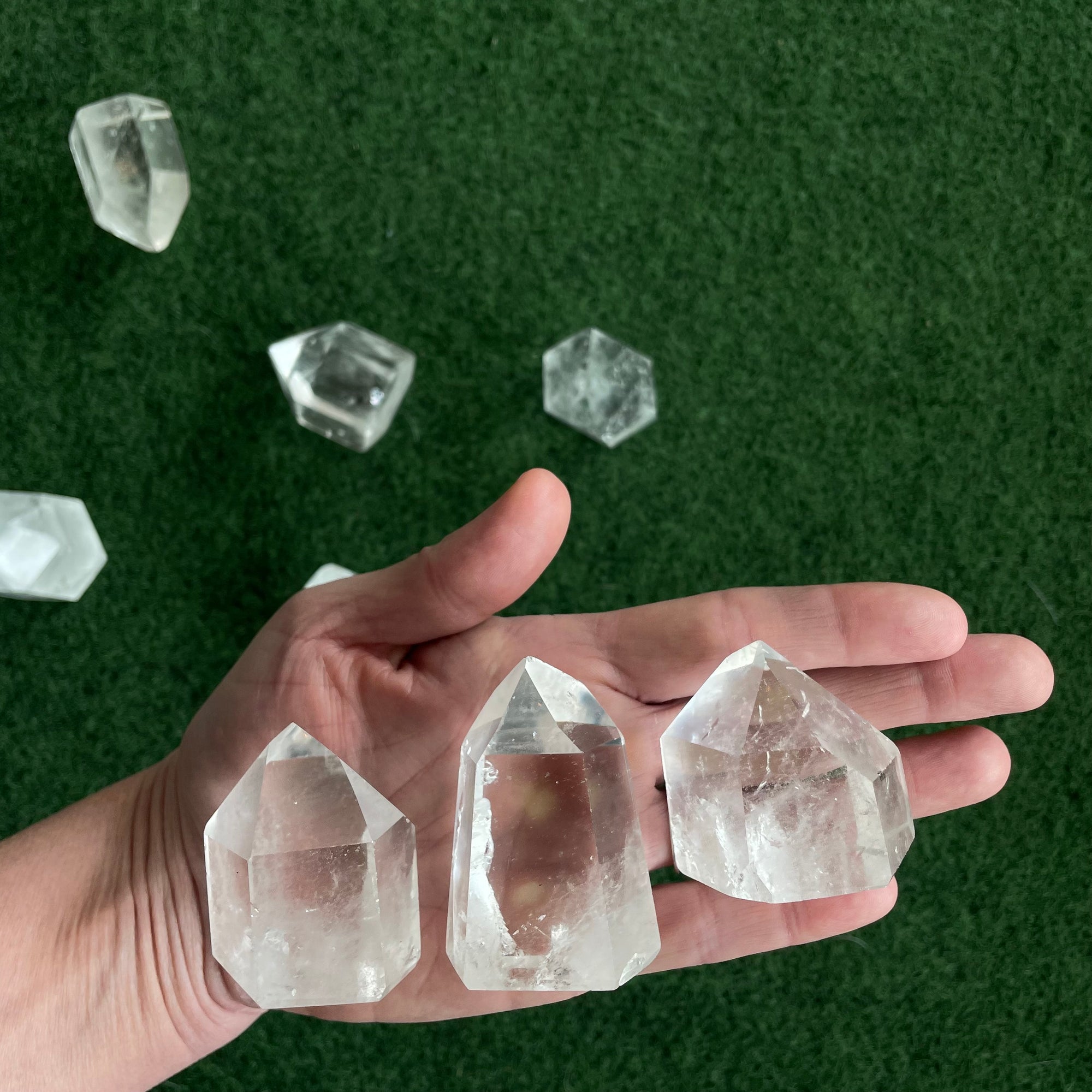 Three crystals are placed in the palm of a person&#39;s hand in front of a green surface. 